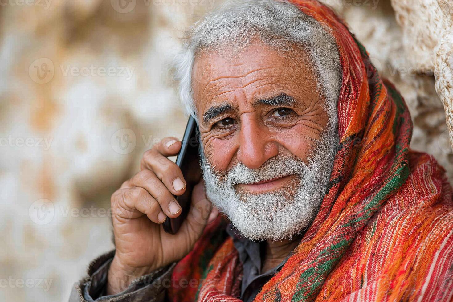An elderly man in national oriental clothing is calling on a mobile phone. He looks at the camera and smiles. photo