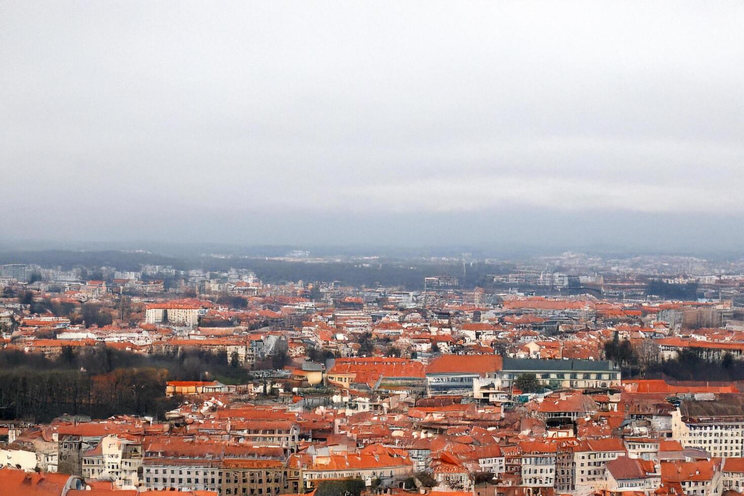 Cityscape aerial view, red roofs, overcast sky, hills background, travel brochure photo