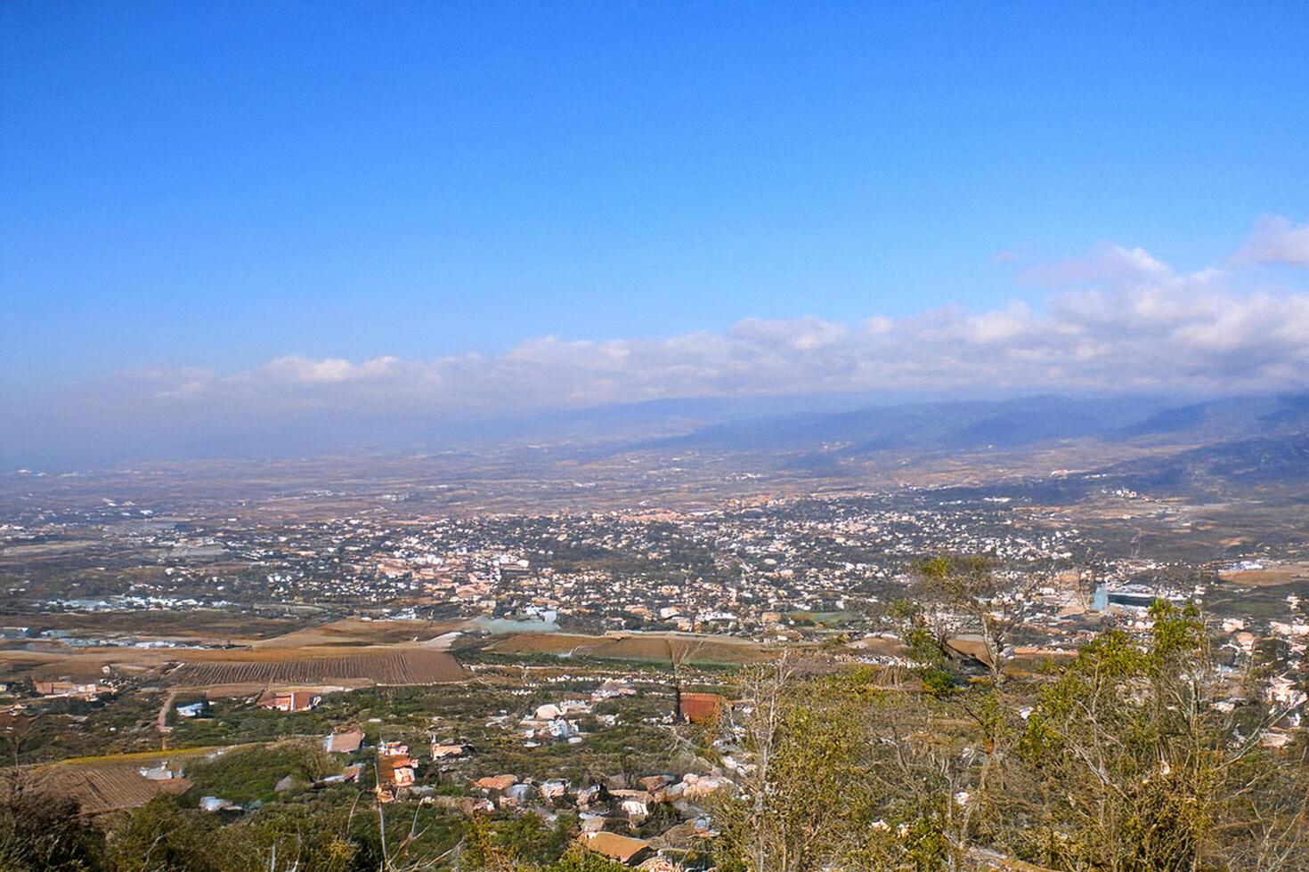 Hilltop panoramic view of city, valley, and mountains under a clear blue sky photo