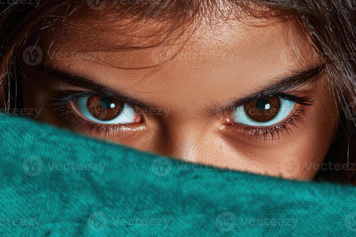 Close up of a girls intense eyes peering from behind a teal fabric photo