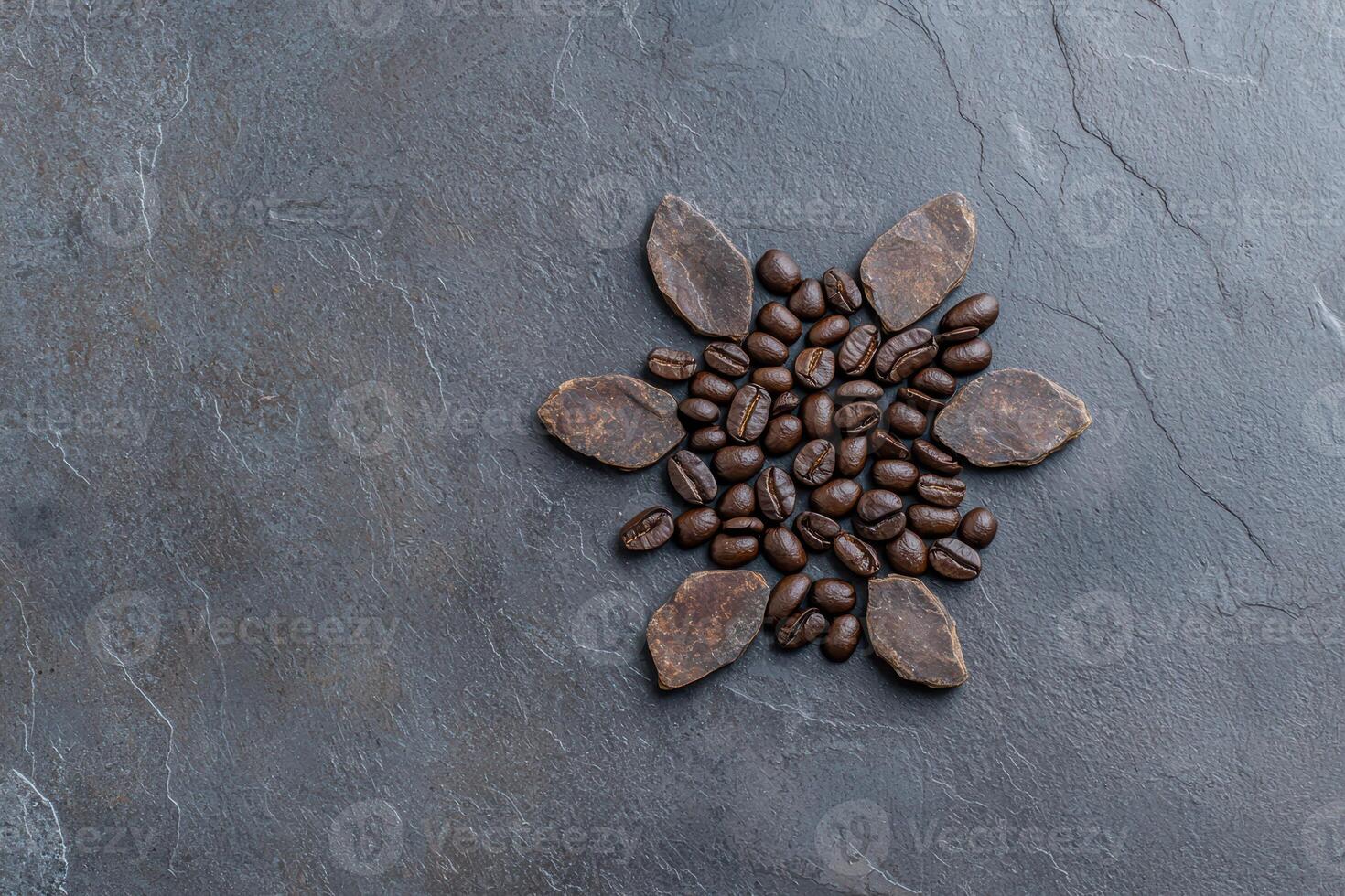 Coffee beans arranged in a sunburst pattern with cocoa pieces on a dark gray slate background photo