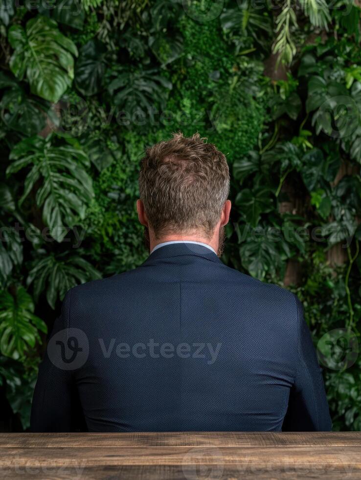Businessman sitting with his back to the camera in front of a green wall photo