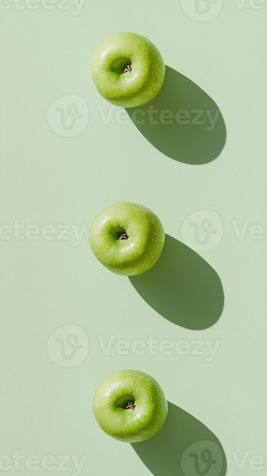 Three fresh green apples casting shadows on a light green background create a minimalist and natural composition. photo
