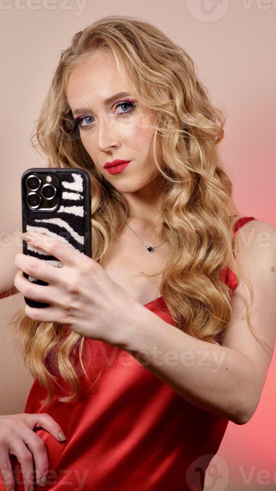 A young woman with red lipstick takes a selfie with long blond hair and makeup. The girl is smiling and looking at the camera close-up photo