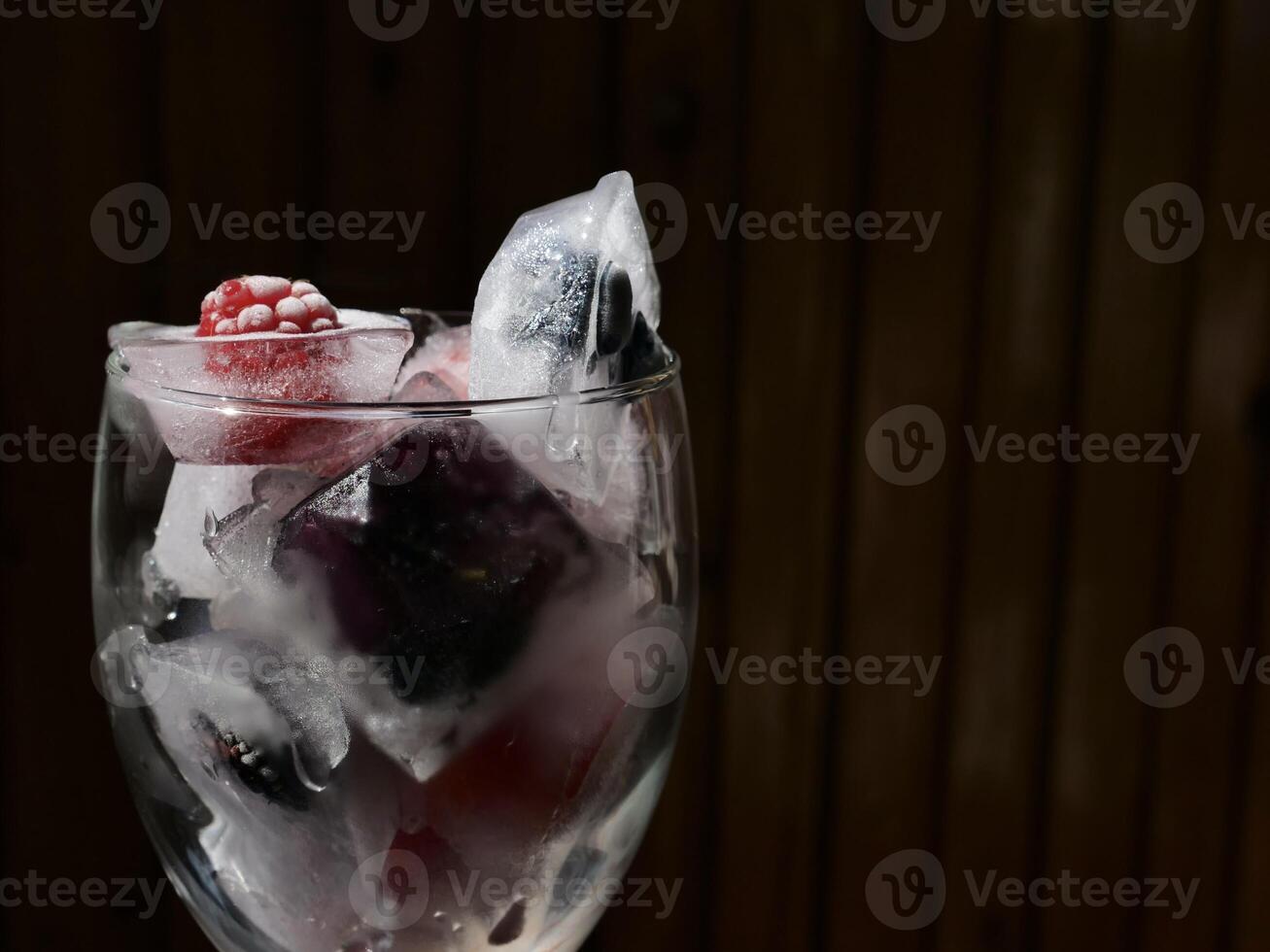 Glass with ice cubes with frozen berries and fruits close-up for a refreshing drink and preservation of seasonal vitamins raspberries, strawberries, cherries, blueberries, mulberries, blackberries photo