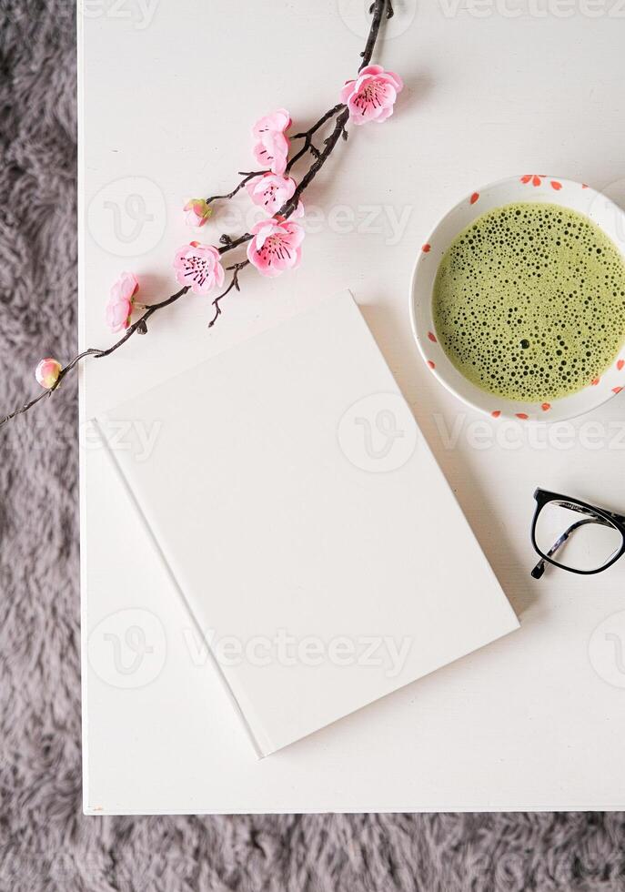 blank book cover mockup on white coffee table with green matcha tea and sakura branch photo