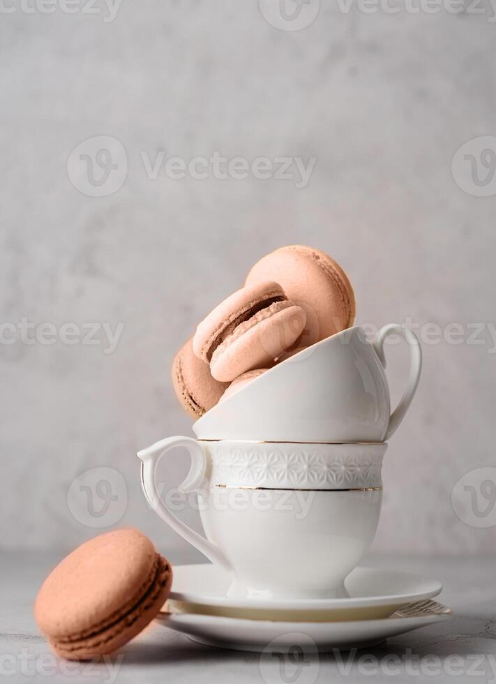 Mocha Mousse - color of the year 2025. Stack of white coffee cups filled with macaroons on the edge of the table, white brick wall background photo