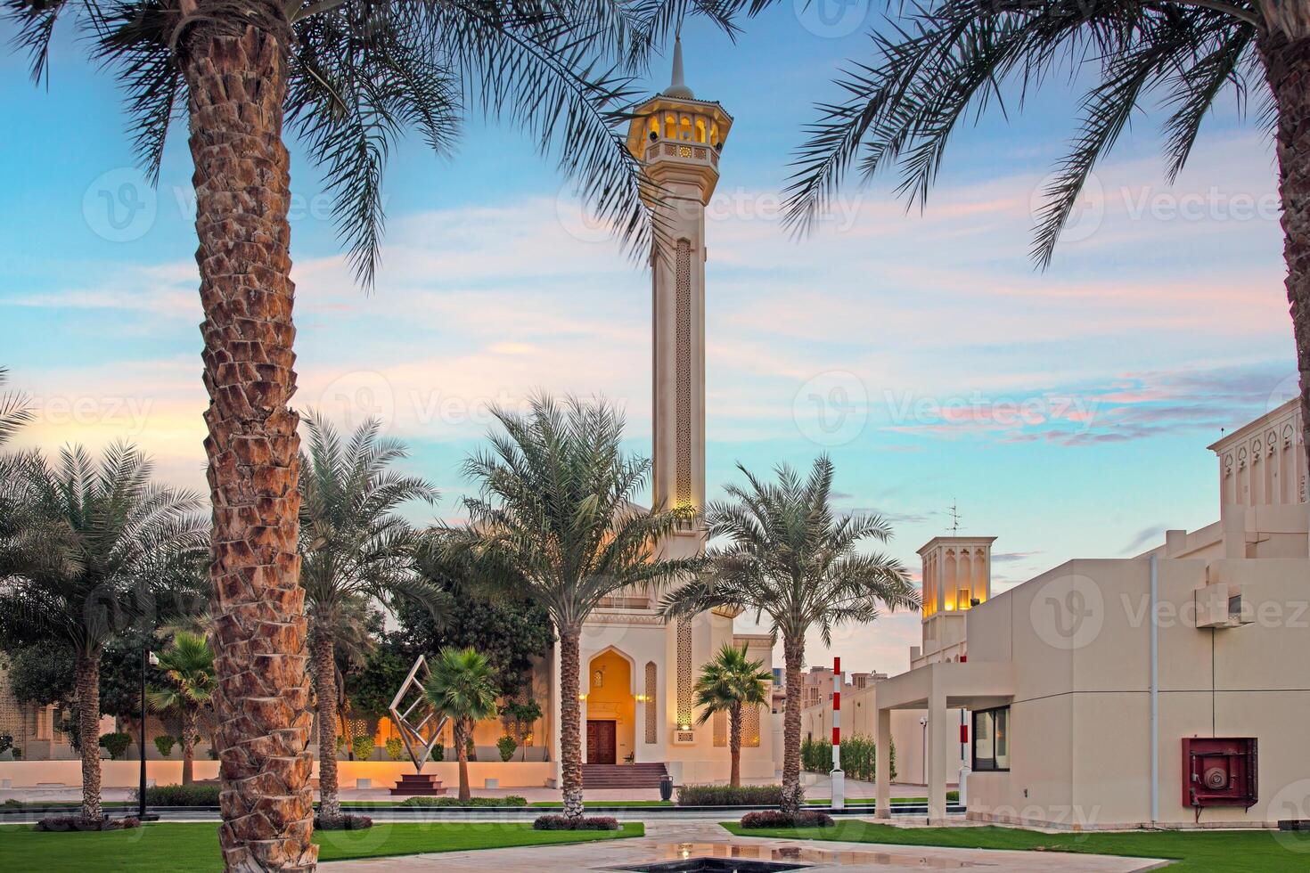 Islamic mosque with tall minaret framed by palm trees at sunset in peaceful courtyard photo