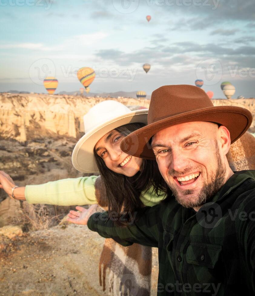 Close up Couple of tourists having fun watching hot air balloons from viewpoint smile to camera in Cappadocia at holiday - Happy friends laughing together on vacation - People and holidays concept photo