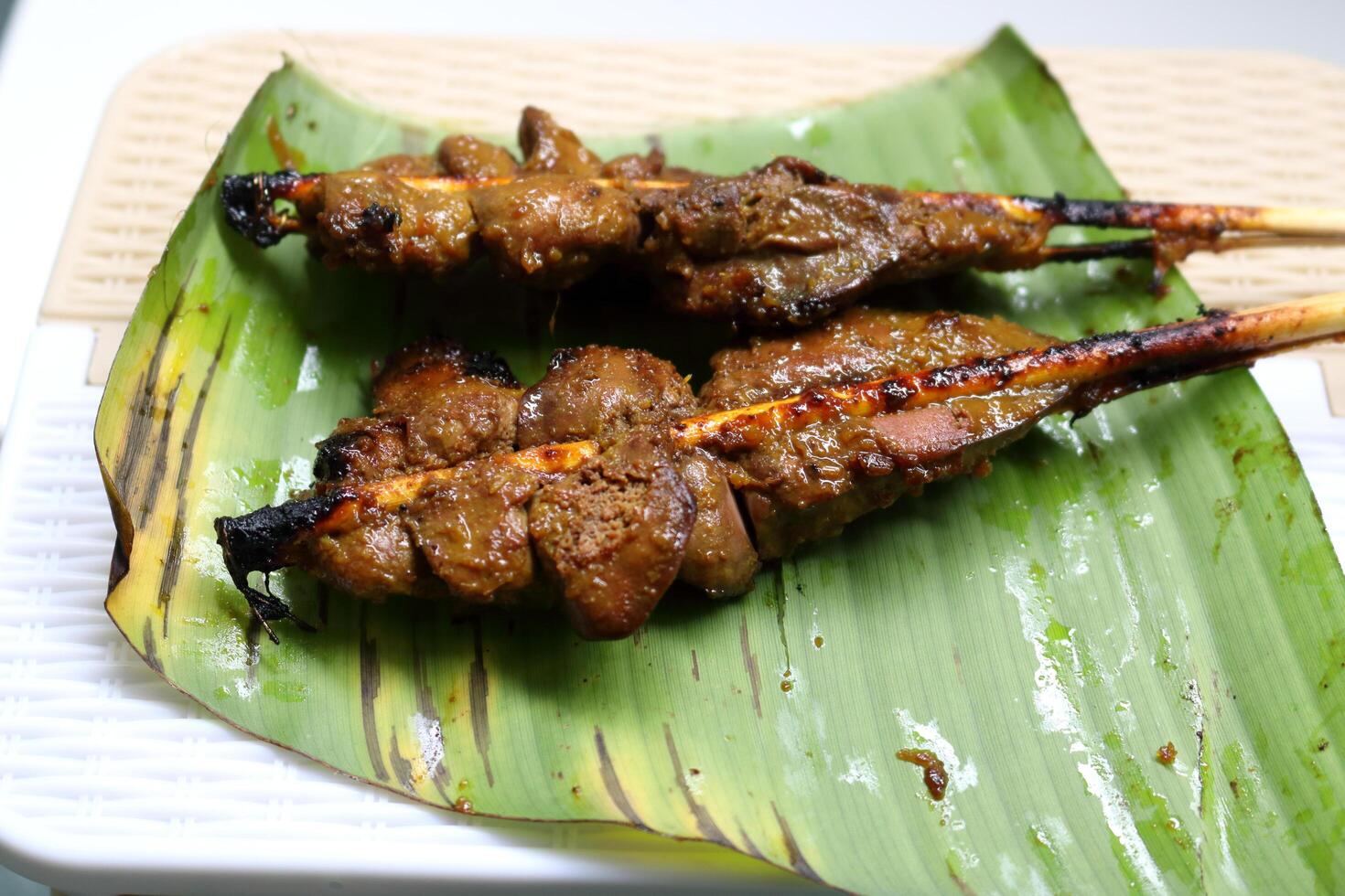 Close up two bamboo stick clamp chicken's livers grilled on banana leaf on table. photo