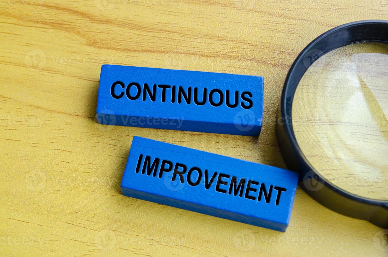 Top view of continuous improvement text on blue wooden blocks with magnifying glass background. Continuous improvement concept photo