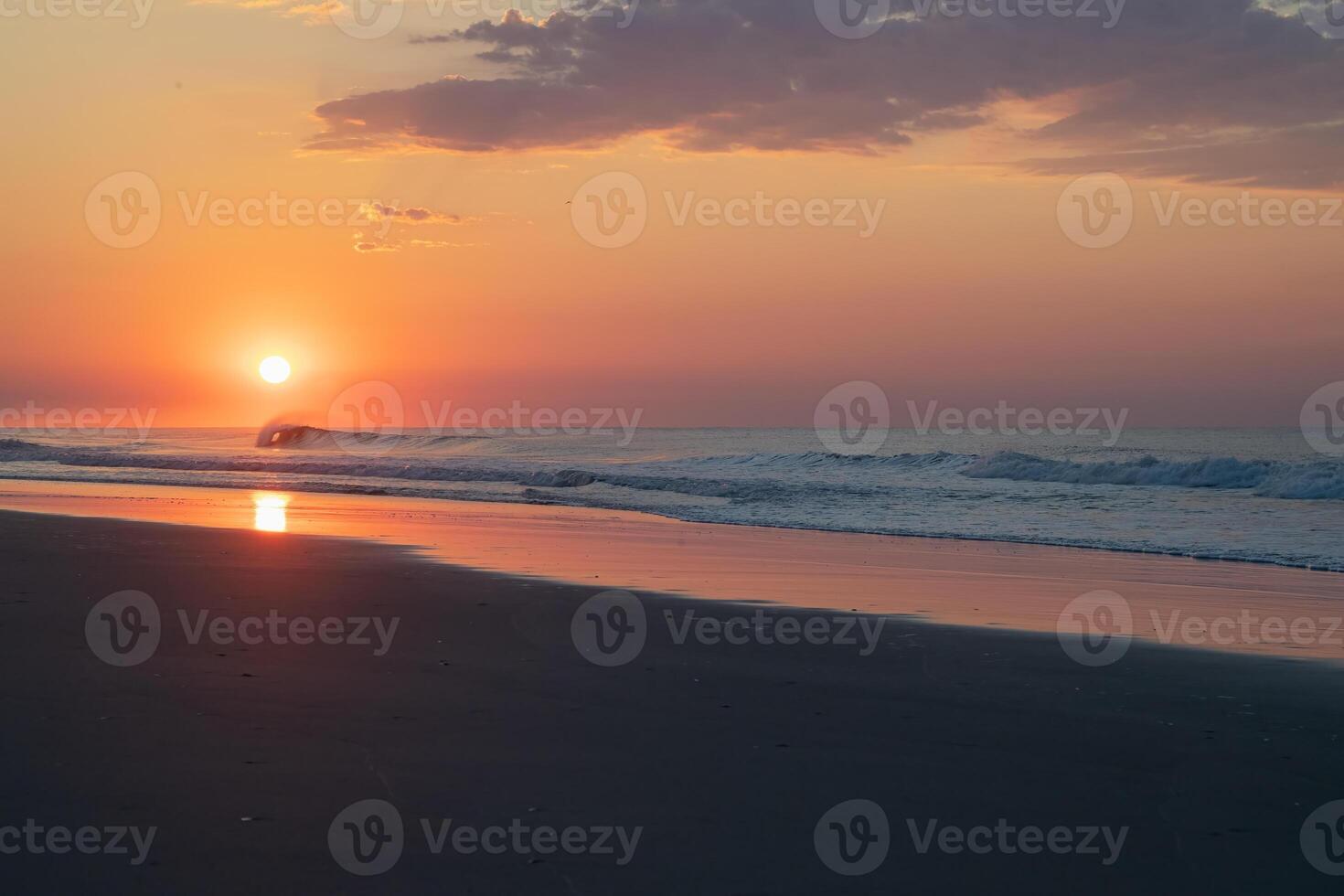 A wave Crashes as the Sun Rises Over the Ocean photo