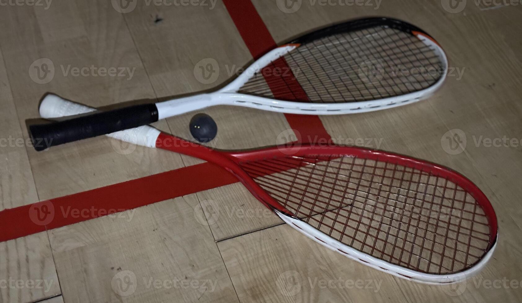 Two rackets and two squash balls lie on the parquet floor. Horizontal photo