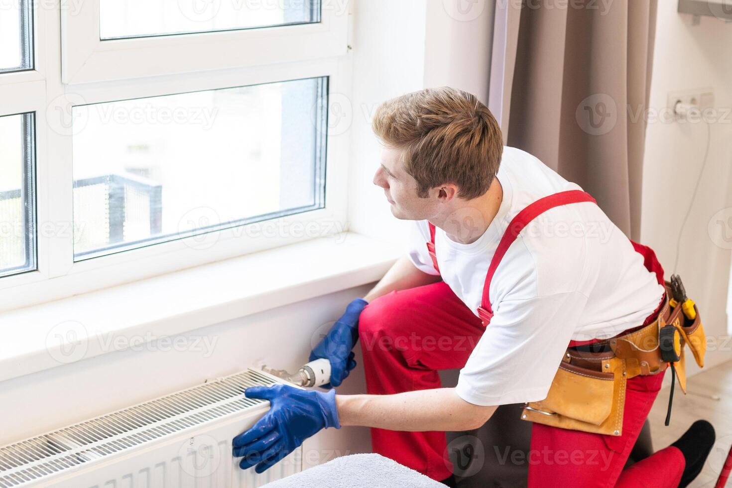 A plumber is fixing a radiator. With an adjustable wrench, he tightens the tap. A briefcase with a tool at hand photo