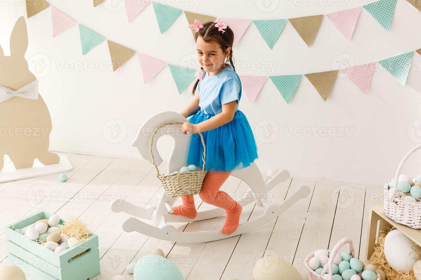 Getting ready to Easter. Lovely little girl holding an Easter egg and smiling with decoration in the background photo