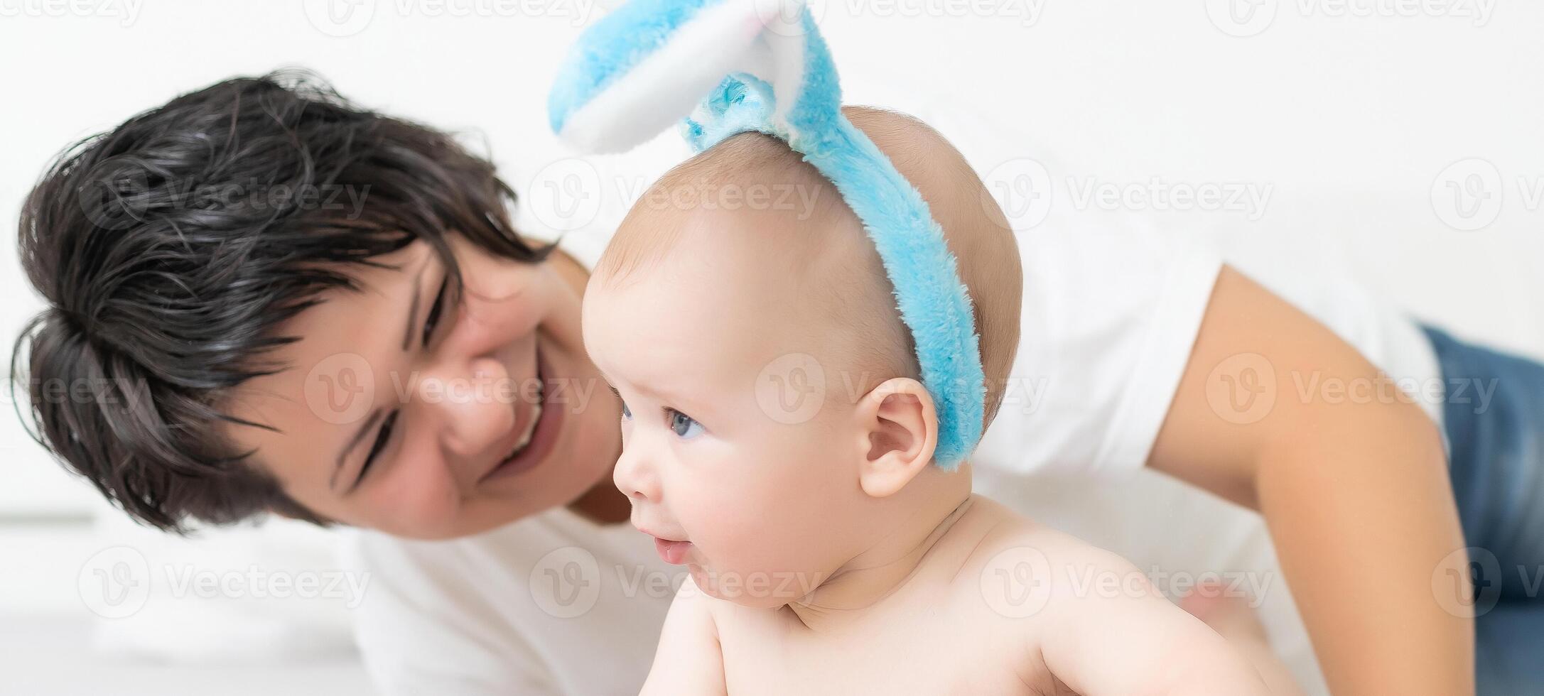 Mother and child with colorful eggs. Mom and baby with bunny ears. Parent and kid play indoors in spring. Family celebrating Easter photo