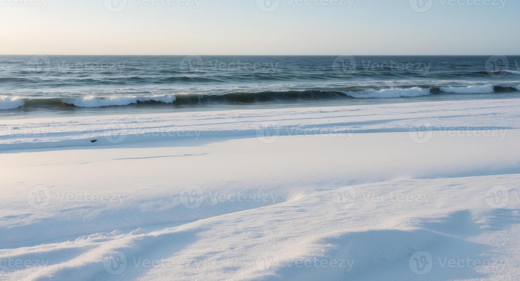 A pristine beach in winter where soft white snow contrasts with the dark blue ocean waves creating a stark and beautiful landscape photo
