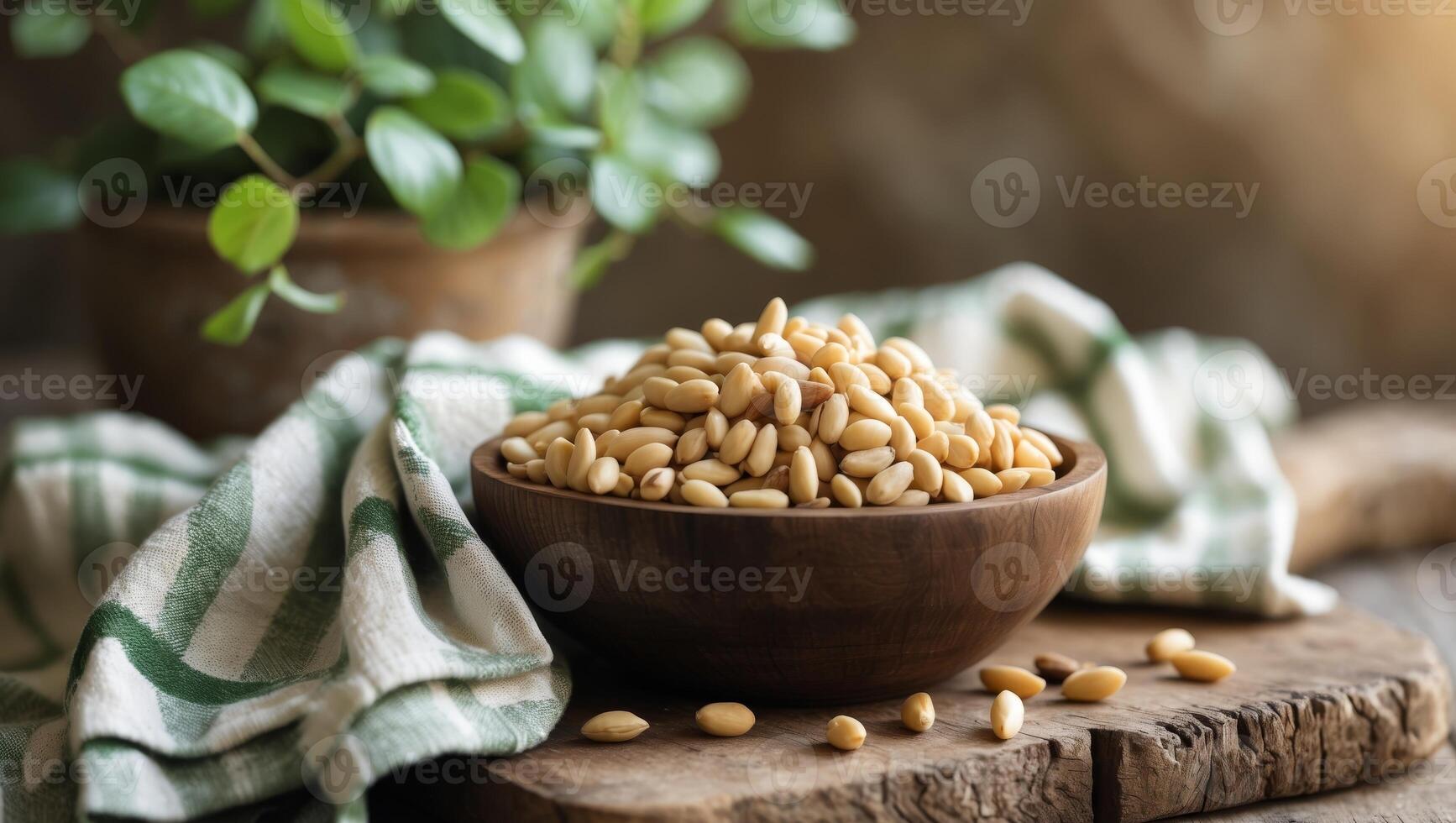 Pine nuts in a wooden bowl on a wooden board with a checkered kitchen towel and a green plant in the background photo