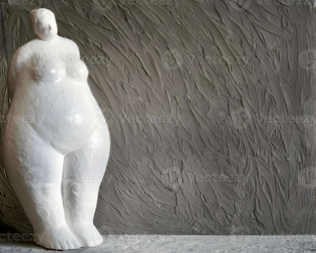 A figurine of a plump woman made of white plaster against a gray background with copy space in a minimalist style. photo