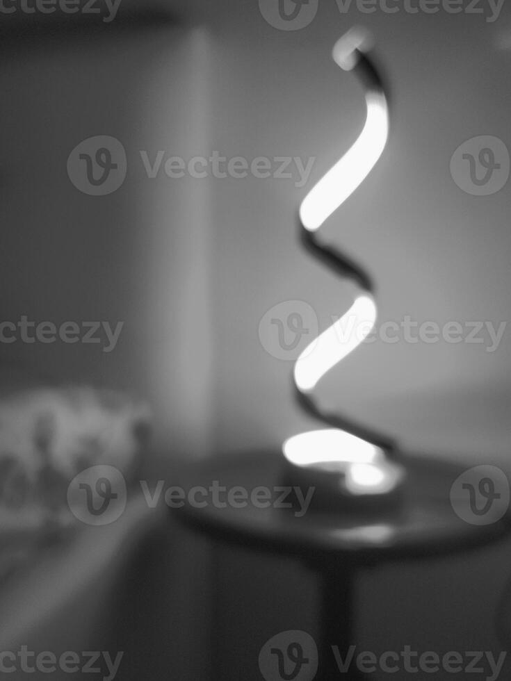 A spiral-shaped lamp on a black bedside table in the style of a blurred black-and-white photograph, Suitable for text overlay photo