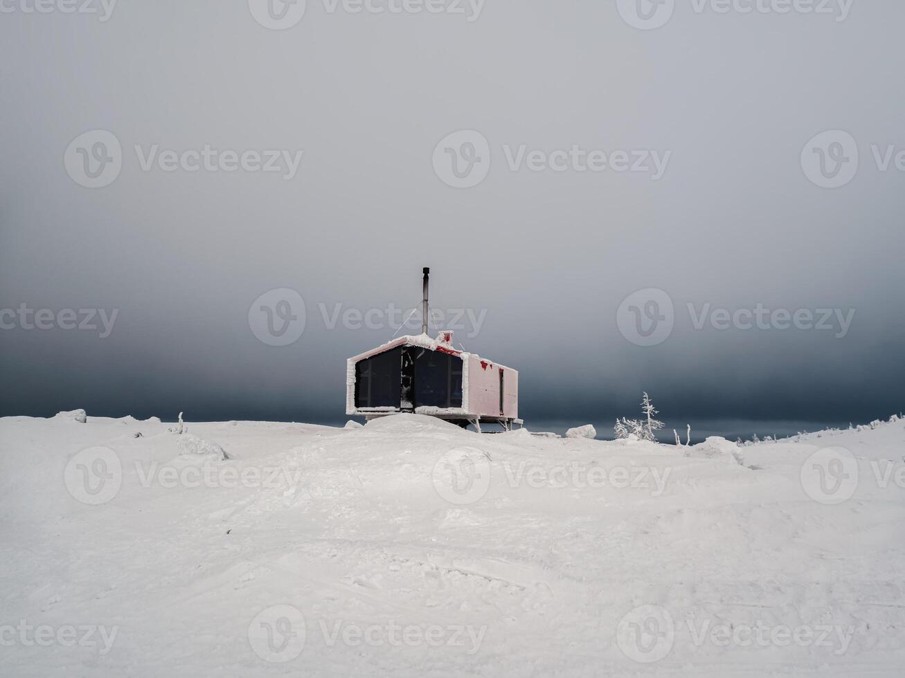 Lonely red guest house on a snow-covered slope in winter under night dramatic sky. Winter shelter for tourists, house on the mountain. photo