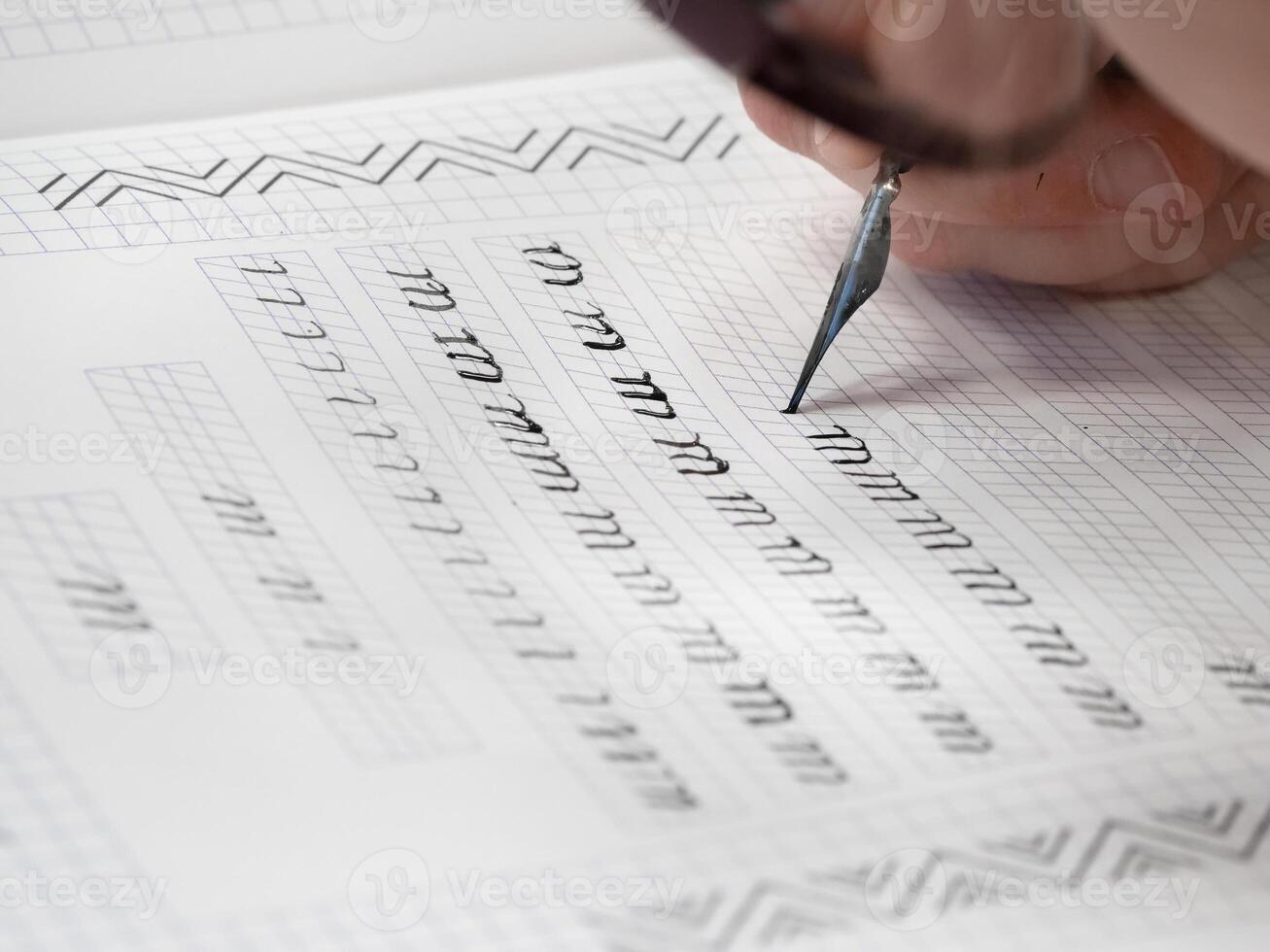 Close-up pupil's hands are writing calligraphy in a notebook. photo