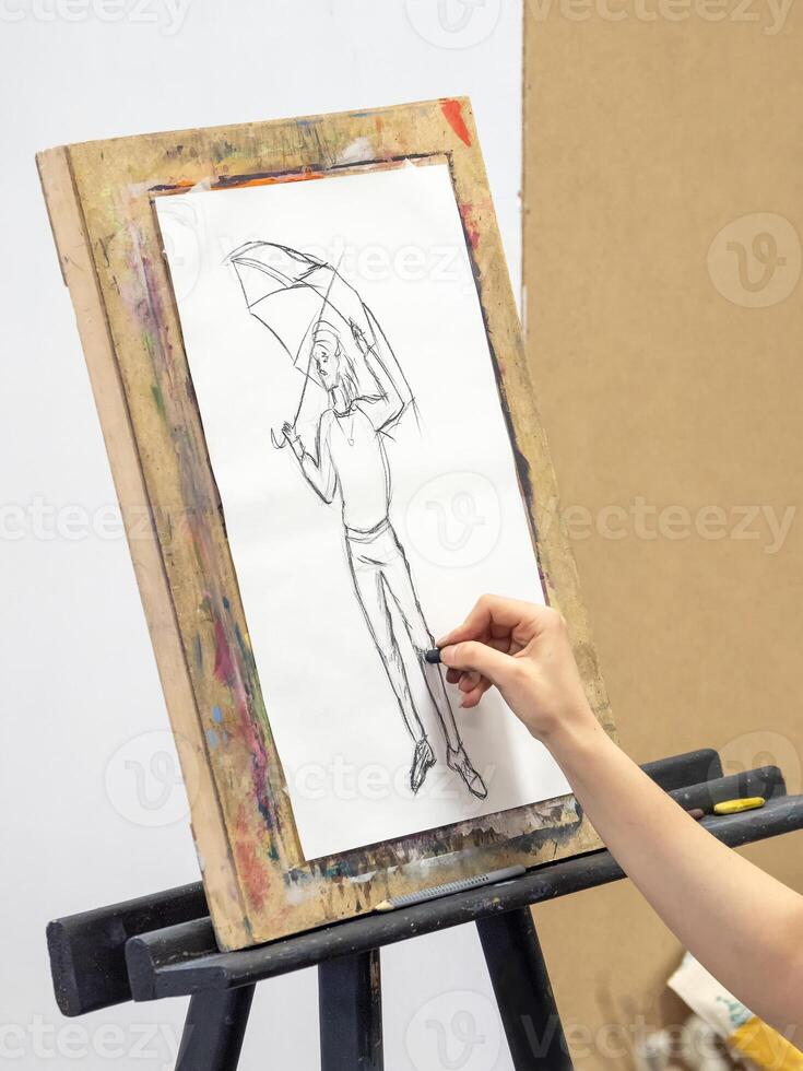 Artist's hand with a black chalk is brought to a white canvas and begins to draw a sketch. photo