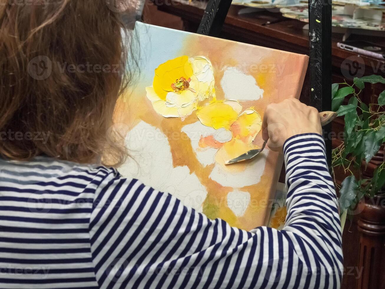 Creative woman drawing texture paste, working with a spatula, creating a three-dimensional drawing of flowers in the picture. photo