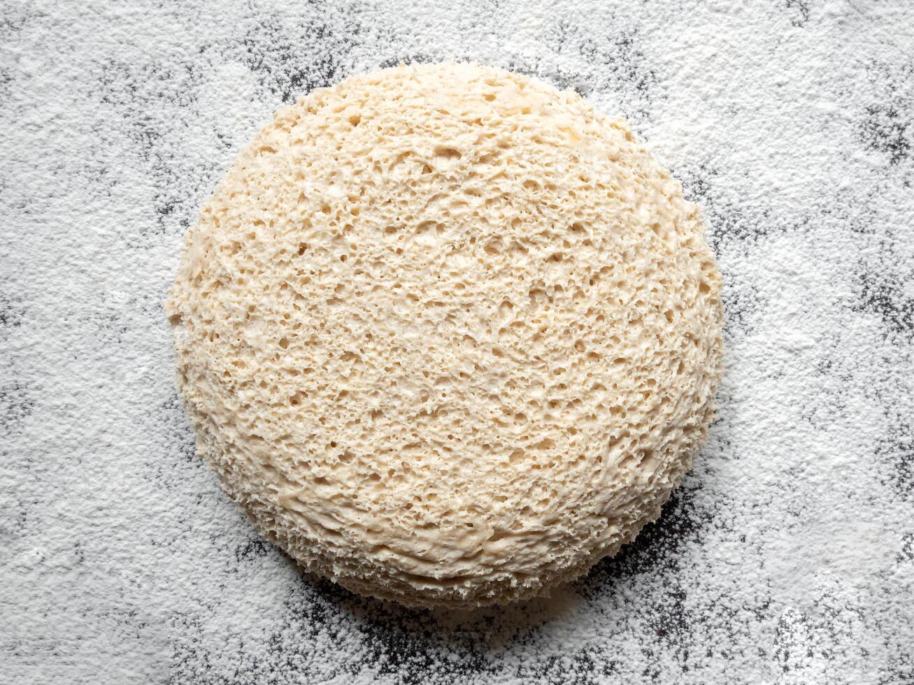 Round piece of yeast-free dough on a floured table. Cellular texture of yeast-free dough. White bread texture. Mankind oldest staple foods. photo