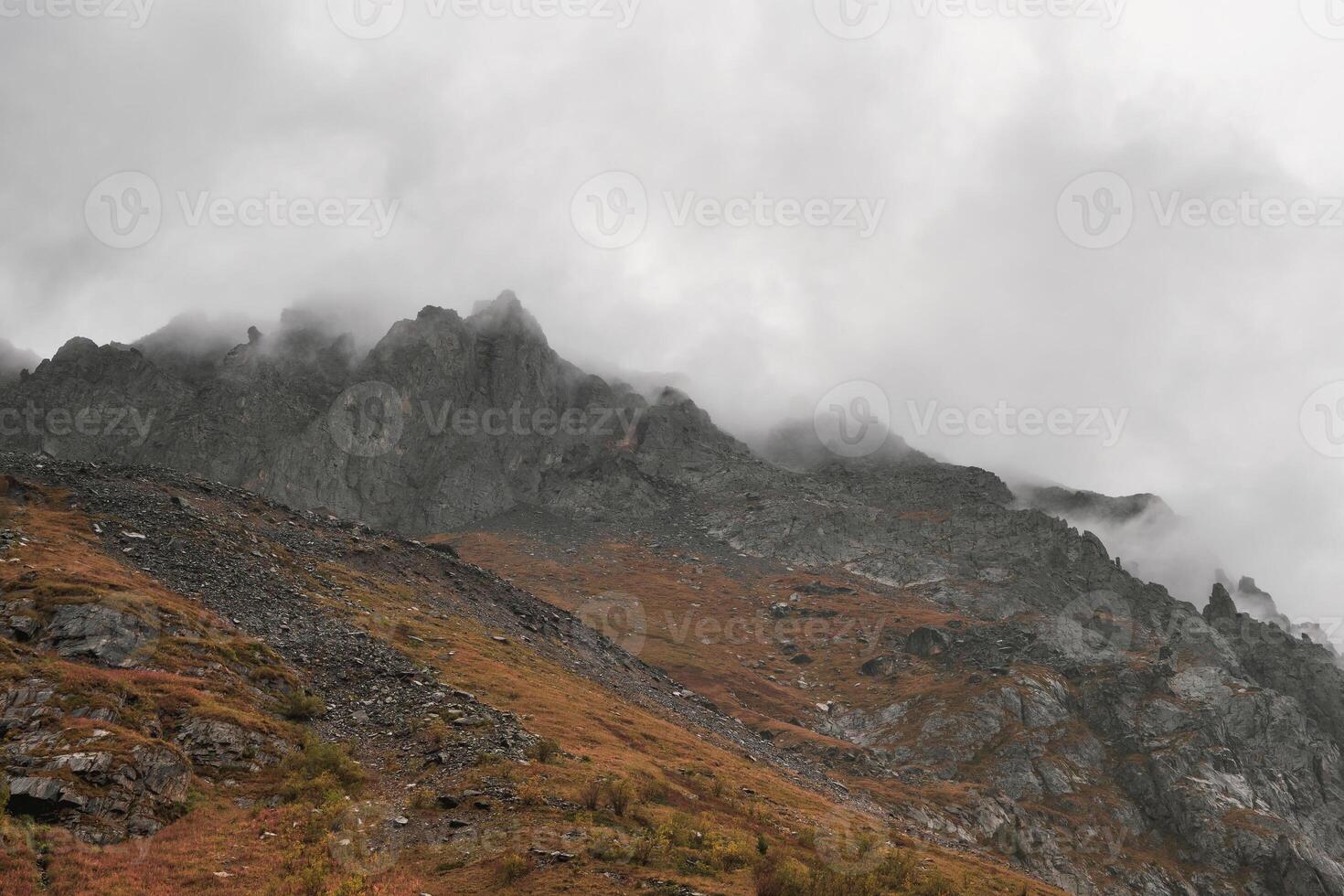 Mystical background with dramatic mountains. Rain in mountains. Atmospheric misty landscape with fuzzy silhouettes of sharp rocks in low clouds during rain. photo