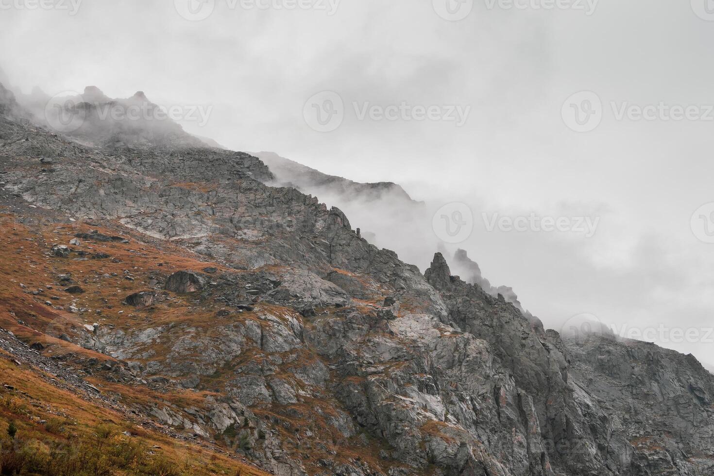 Atmospheric misty landscape with fuzzy silhouettes of sharp rocks in low clouds during rain. photo
