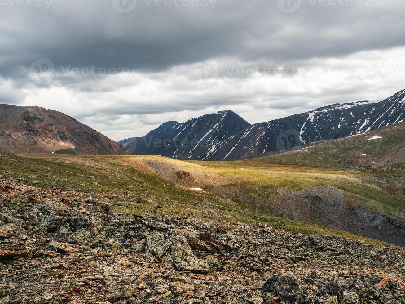 Scenic landscape with sunlit mountain pass under clouds in rainy day. Colorful mountain in sunlight. Motley scenery with stone hills under cloudy sky in changeable weather. photo
