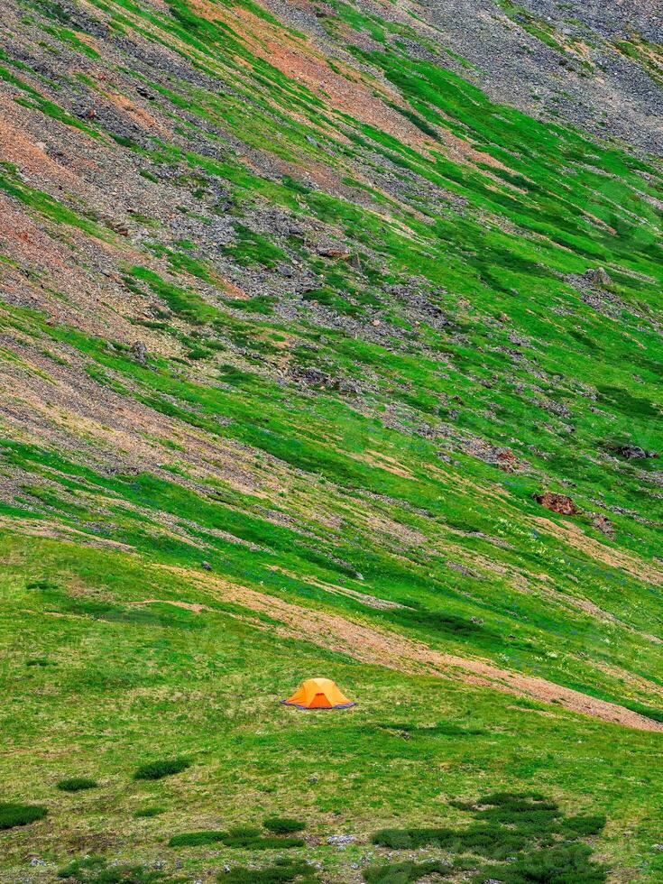 Tourist tent far away on a green mountain slope. Minimalistic landscape of a green mountain slope with a small tent. Scenic alpine landscape with tent on green hill among rocks. photo