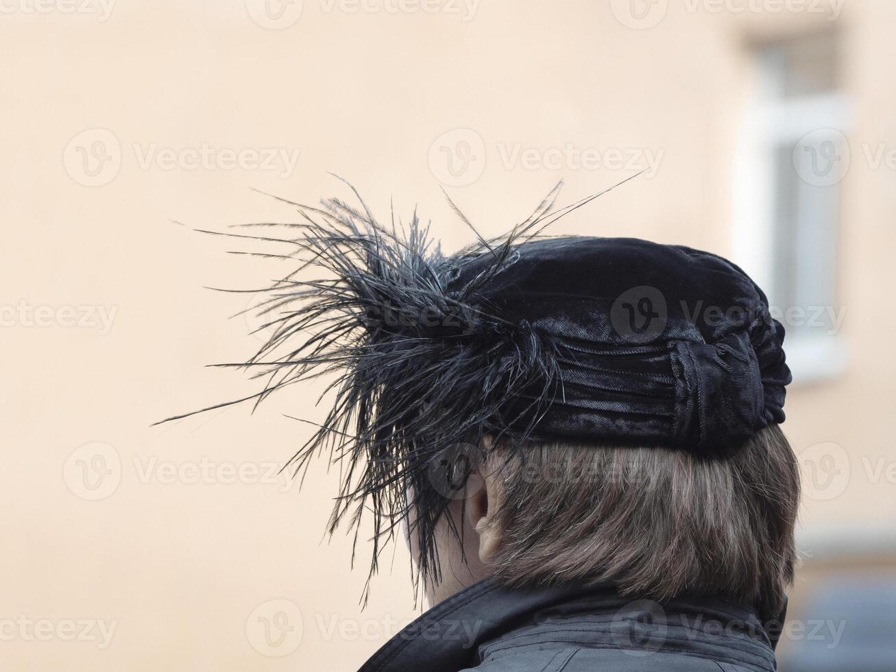 Back view of the woman with black hat with feathers on the head in a open air photo