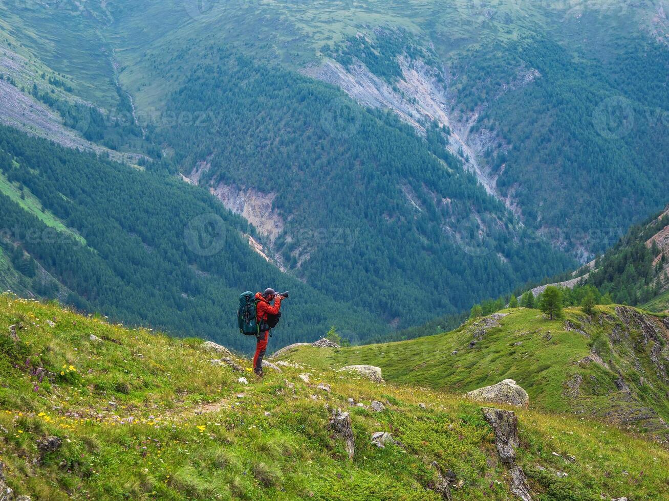 Photographer with a large camera takes pictures of a beautiful mountain landscape. Photographer with a large backpack on a narrow mountain path. photo