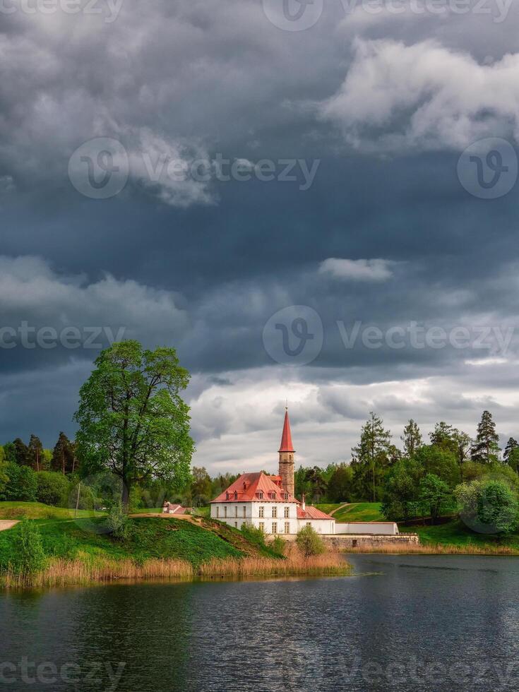 Dark storm over an ancient Maltese castle. Spring park landscape before the rain. State Museum Reserve Gatchina. Russia. Vertical view. photo