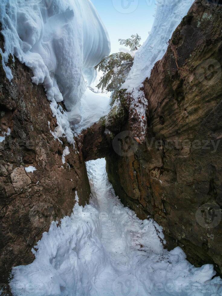 Narrow path through snow drifts between rocks, a stone vault, a cave. photo