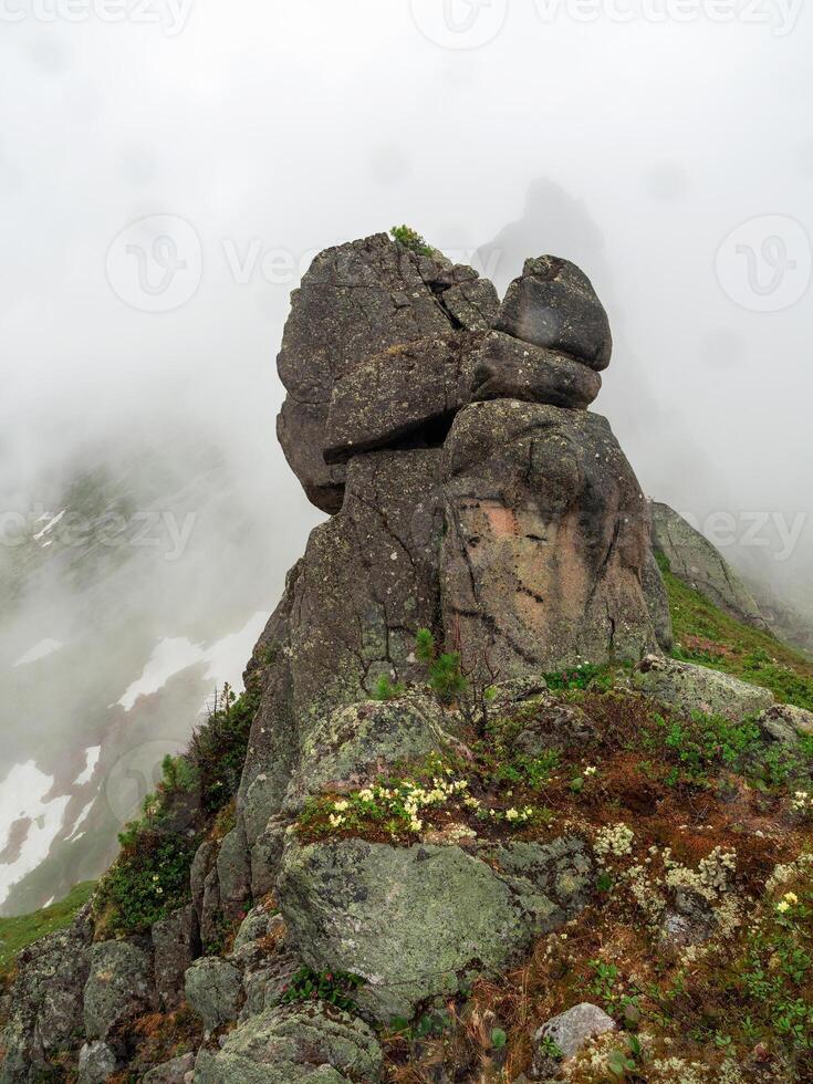 Mountain vertical view from cliff at high altitude. Mystical landscape with beautiful sharp rocks near precipice and couloirs in low clouds. Mountain foggy scenery on abyss edge with sharp stones. photo