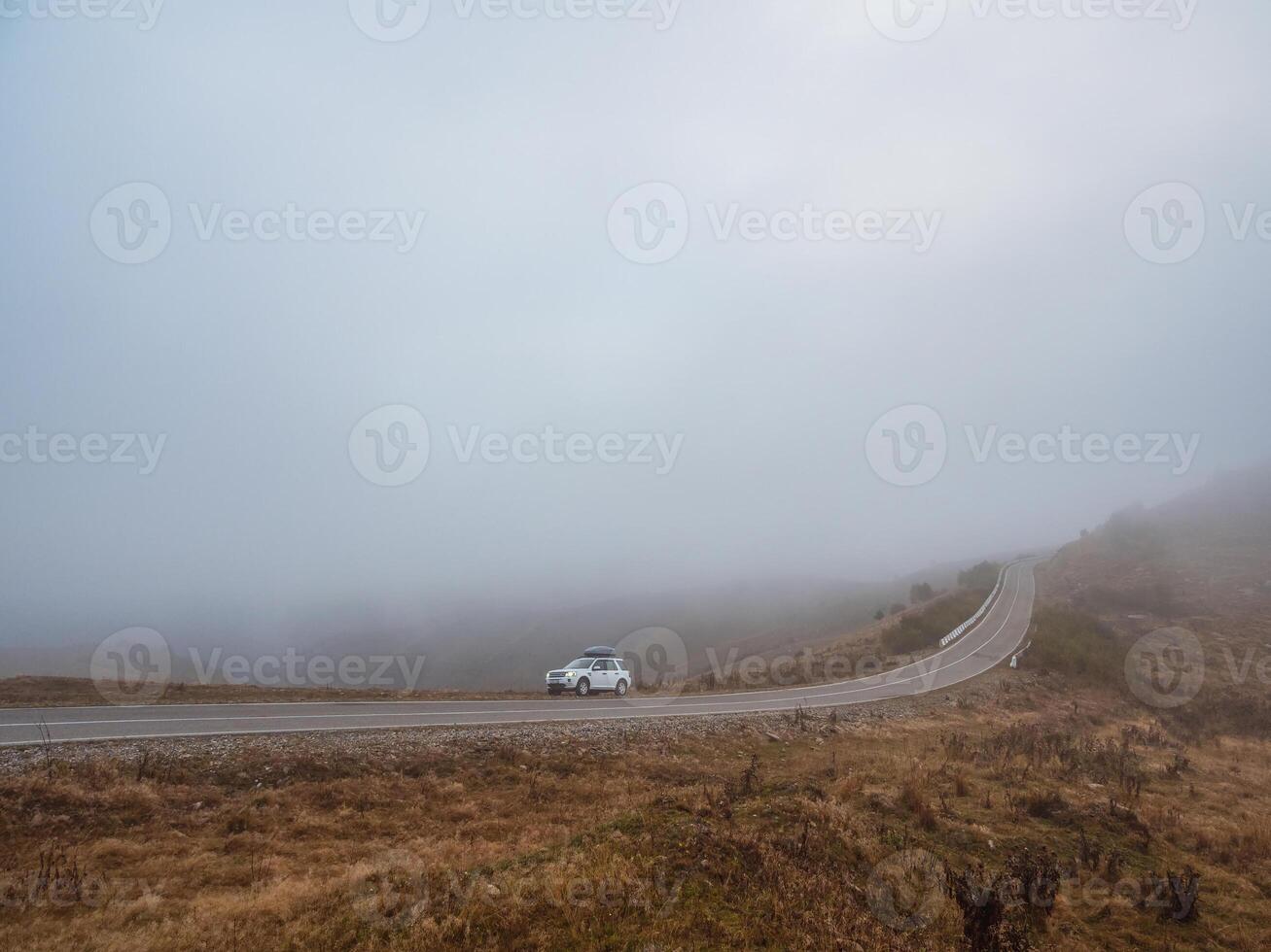Morning mountain highway in dense fog. White car SUV with fog photo