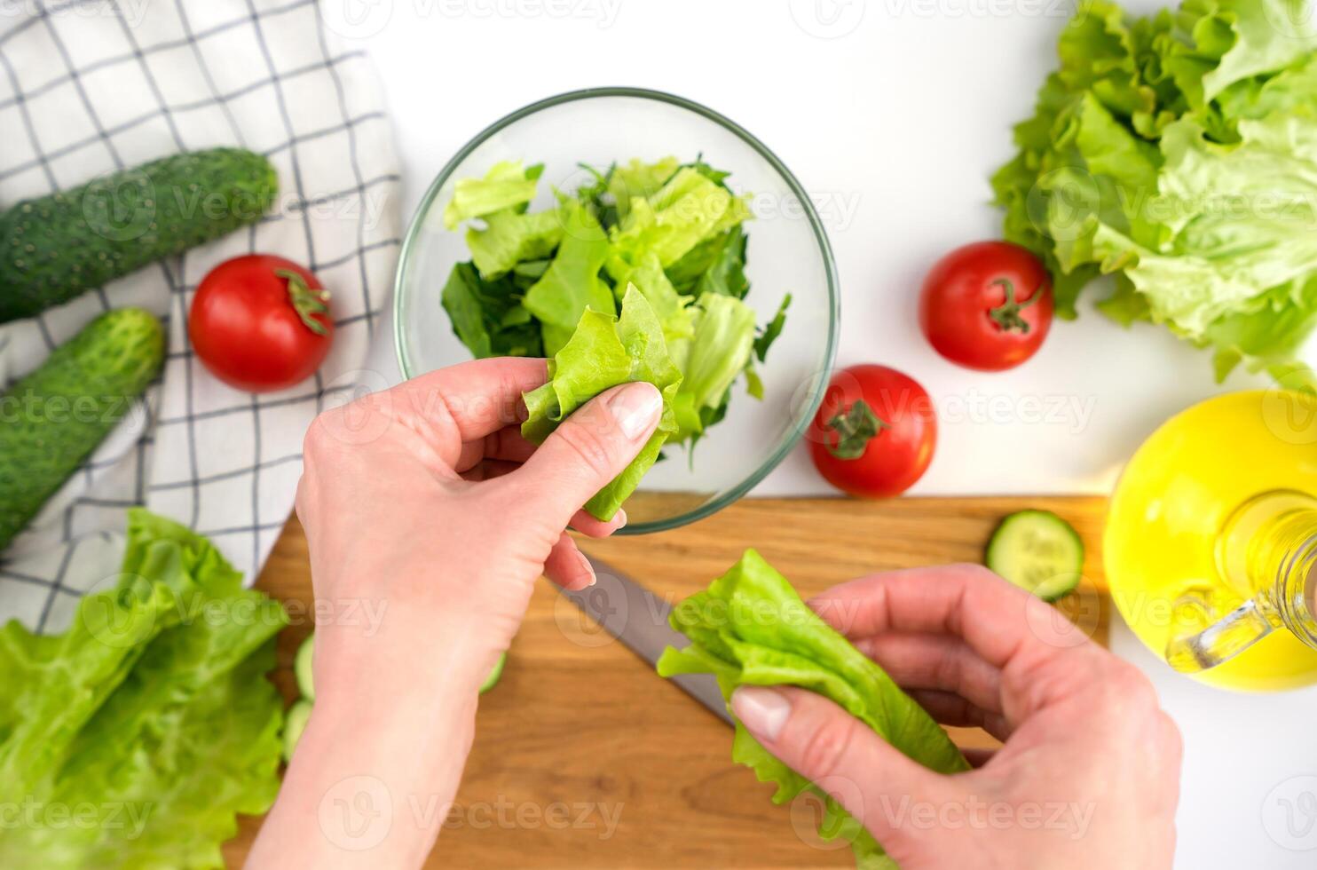 Woman's hands puting lettuce leaves in a glass bowl. Cooking vegetable salad. Close-up. Top view. Selective focus. photo