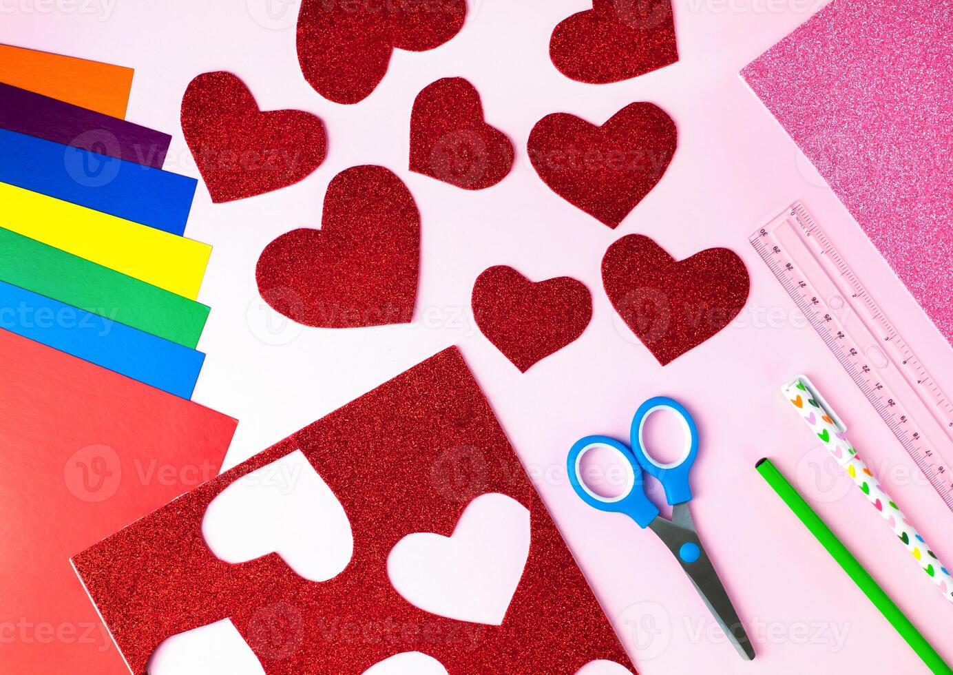 Red paper hearts, color papers, scissors, ruler, pen and pencil for Valentine's day card crafts on pink background. Top view. Flat lay. Step by step photo instruction. Step 3.