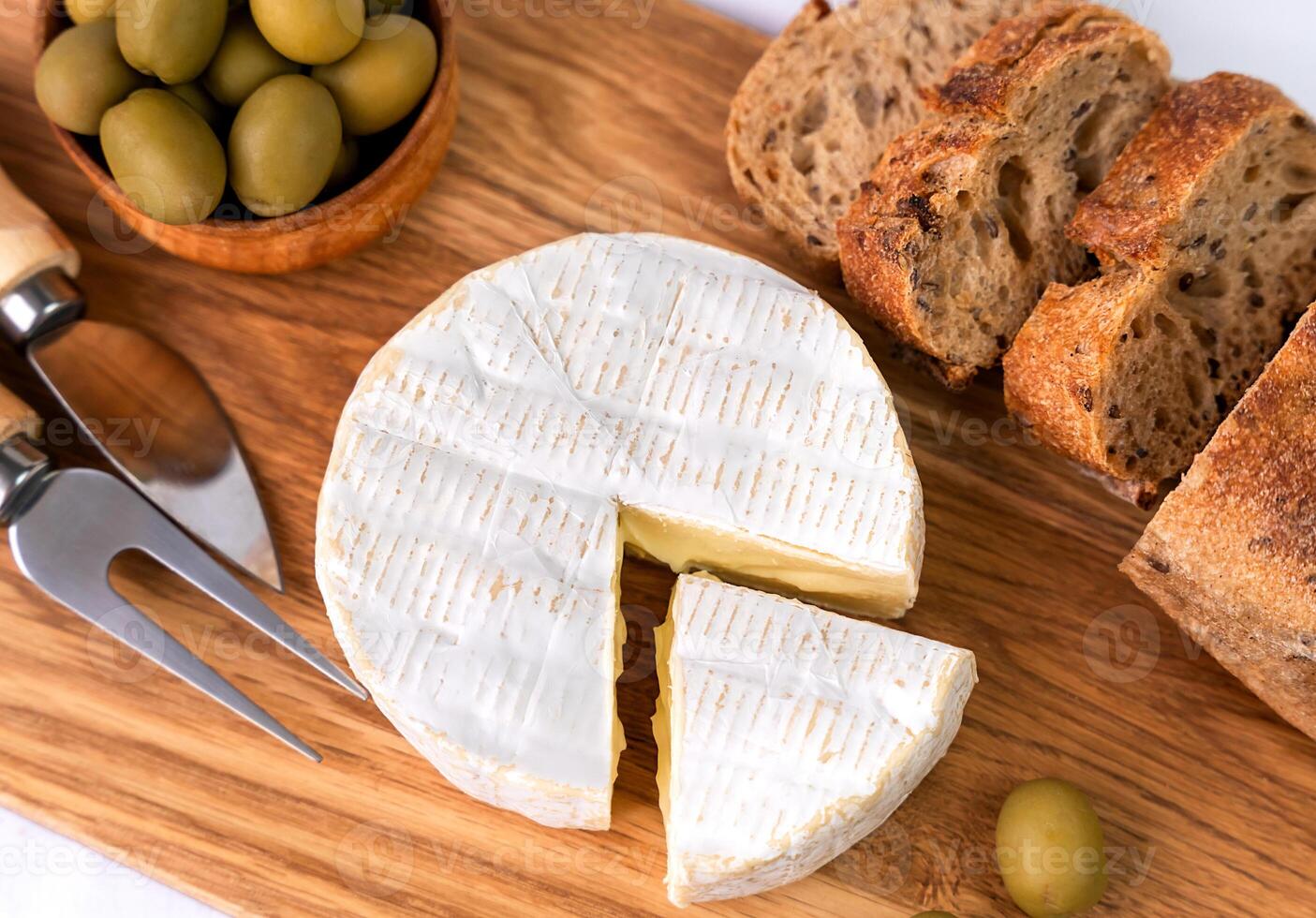 Camembert cheese, fresh baguette, olives on a wooden board. Top view. Close-up. Selective focus. photo