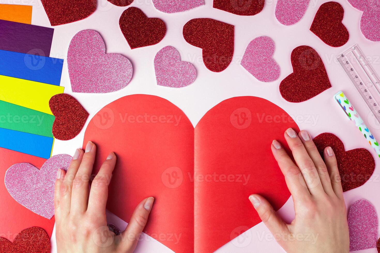 Woman's hands holds a big red paper heart. DIY concept for Valentine's day card crafts. Top view. Flat lay. Step by step photo instruction. Step 8.