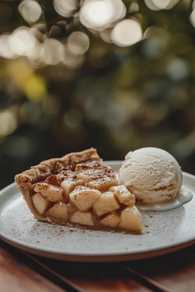 A slice of delicious apple pie with ice cream on white plate, placed on wooden table, blur bright outdoor background photo