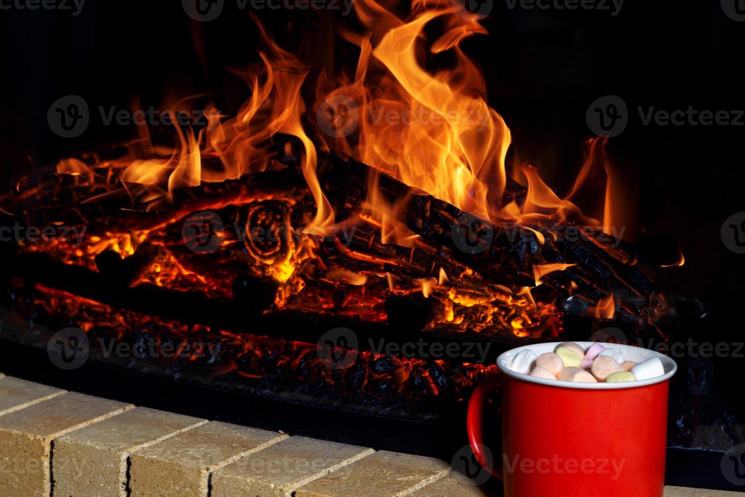 red mug filled with a warm, sweet Christmas drink topped with marshmallows stands out against the shimmering backdrop of a cozy fireplace photo