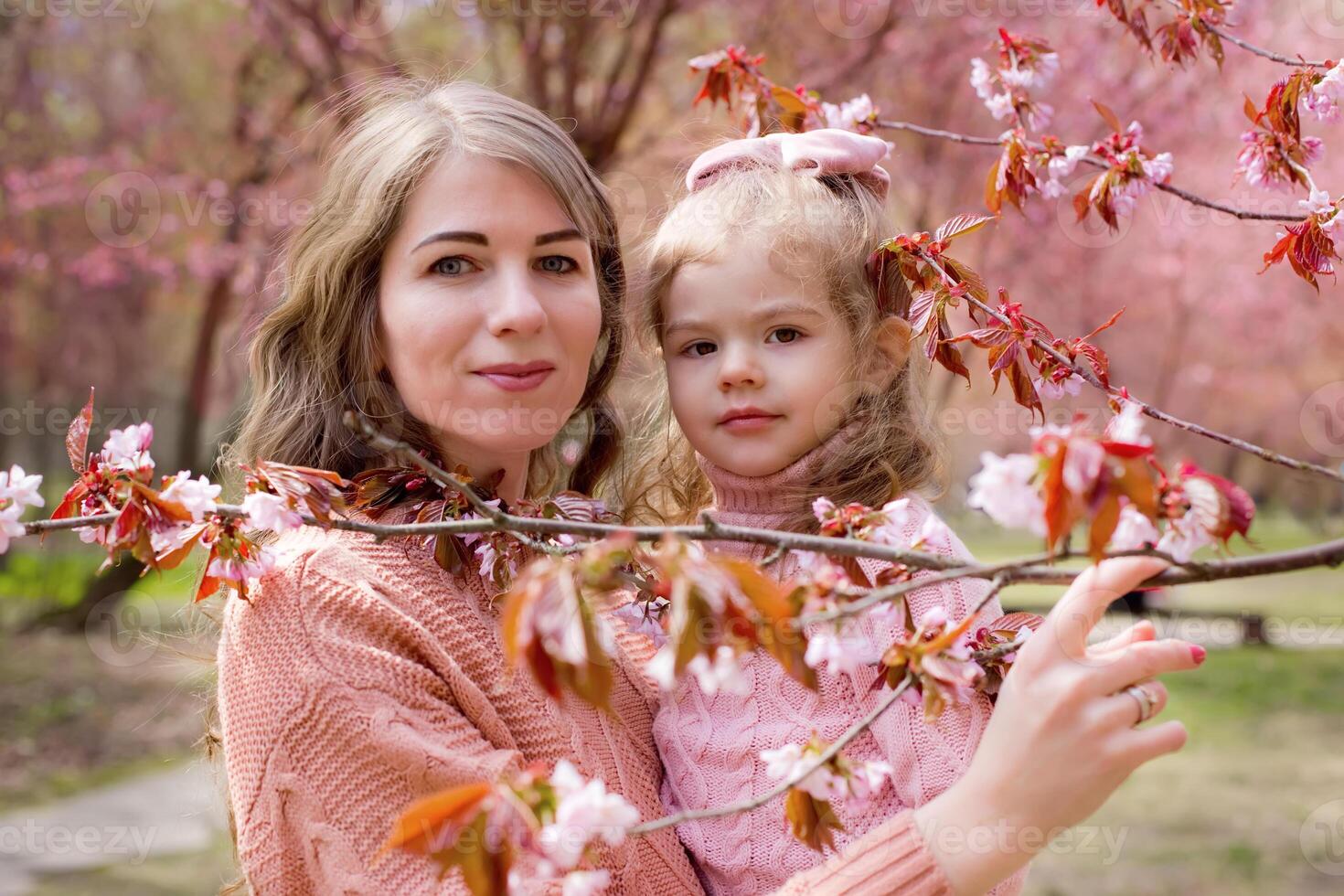 Portrait of mother and daughter in the park with blooming pink sakura photo