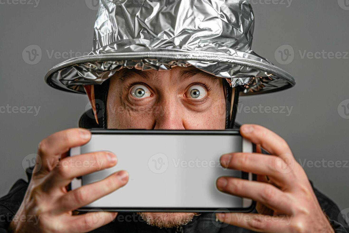 Man with tinfoil hat staring at smartphone in paranoia concept photo