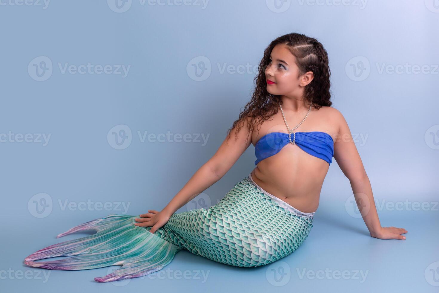Pretty girl in a mermaid costume, isolated on a blue background, looking away photo