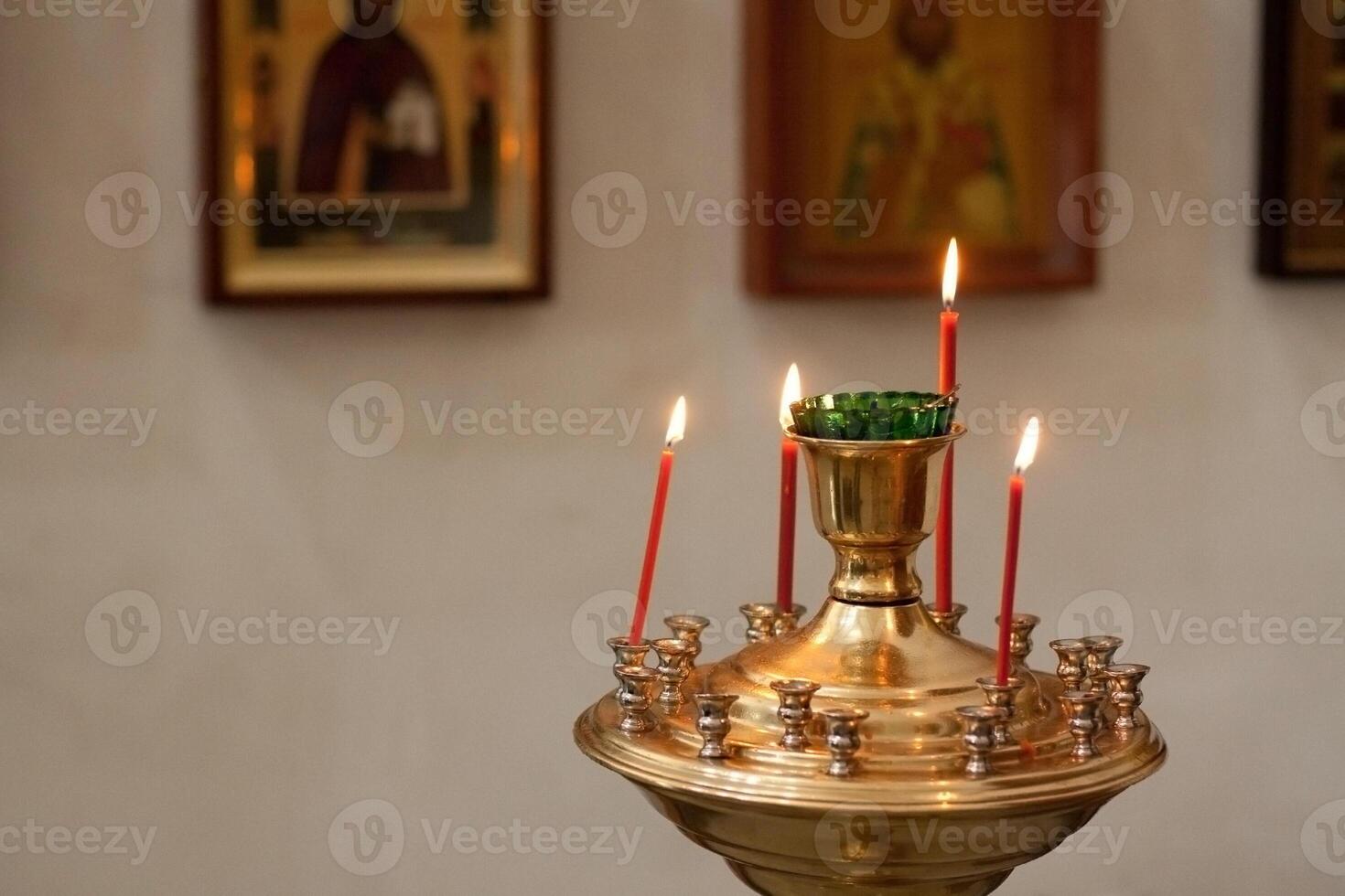 Lit candles in ornate metal holder with religious icons in background photo