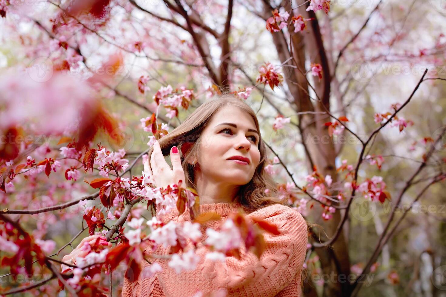 Beautiful woman standing under pink blossom tree in spring park photo